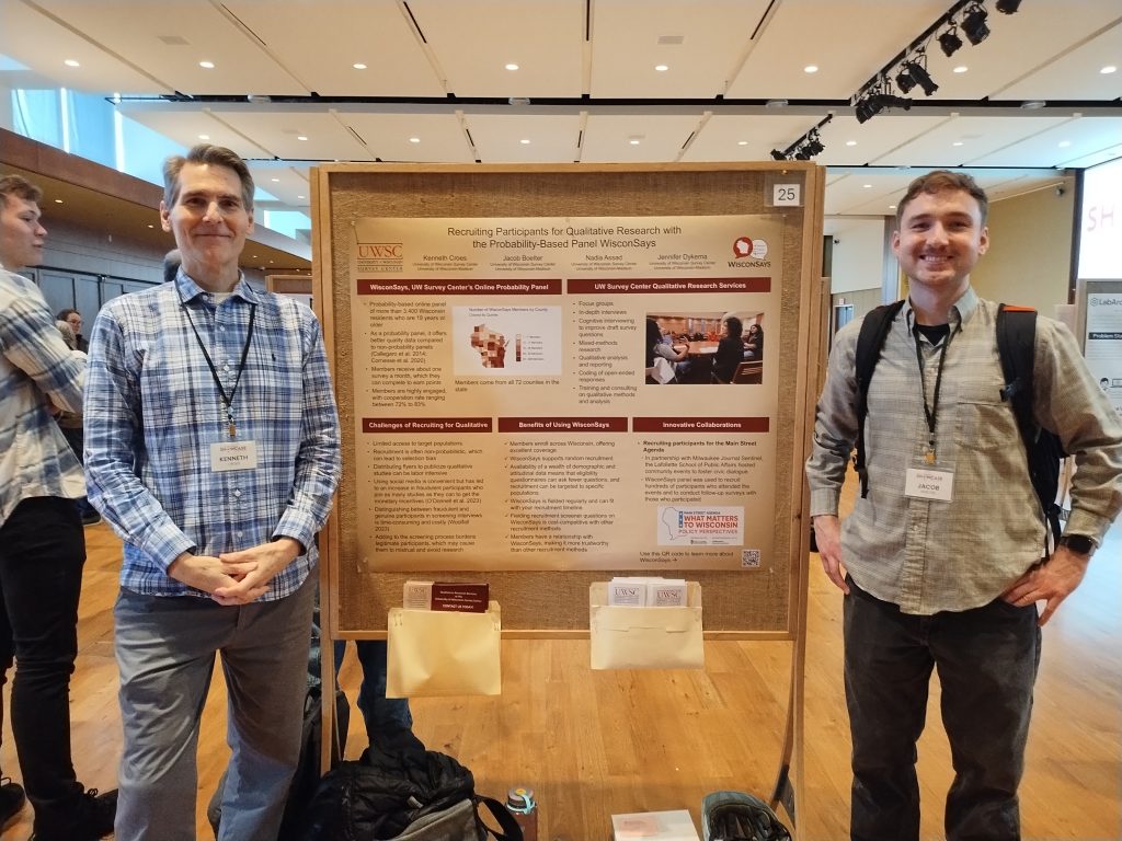 Ken Croes and Jacob Boelter smile next to a board with a poster titled "Recruiting Participants for Qualitative Research with the Probability-Based Panel WisconSays